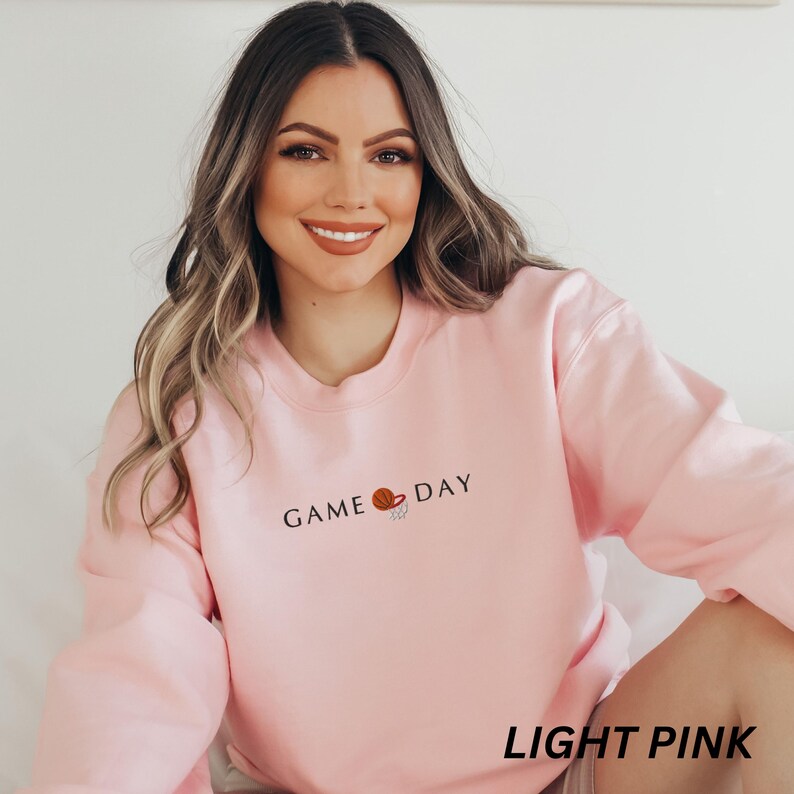 May include: Light pink sweatshirt with the text "GAME DAY" and a basketball graphic. The words "LIGHT PINK" are printed at the bottom of the image. The sweatshirt is a crew neck style.