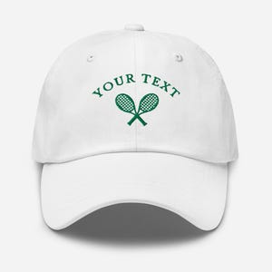 May include: White baseball cap with green embroidered tennis rackets and the text "YOUR TEXT" above the rackets.