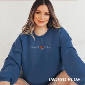 May include: Indigo blue sweatshirt with the words "GAME DAY" and a basketball graphic embroidered on the front. The sweatshirt is a solid color and has long sleeves. The text "INDIGO BLUE" is printed at the bottom of the image.