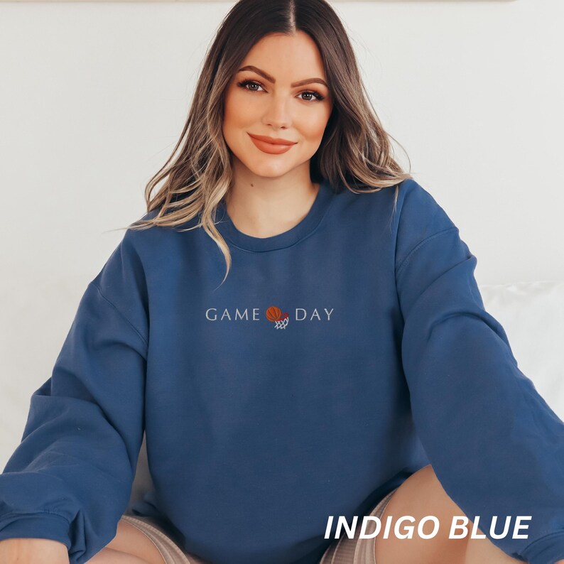 May include: Indigo blue sweatshirt with the words "GAME DAY" and a basketball graphic embroidered on the front. The sweatshirt is a solid color and has long sleeves. The text "INDIGO BLUE" is printed at the bottom of the image.