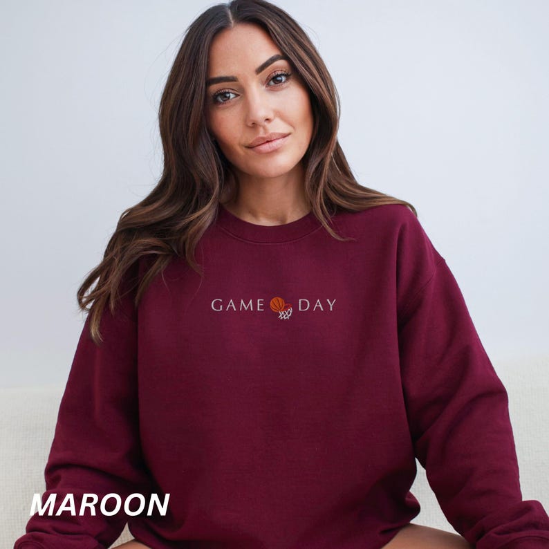 May include: Maroon sweatshirt with the text "GAME DAY" and a basketball graphic. The sweatshirt is a solid maroon color and has a crew neck. The text and graphic are in white and orange.