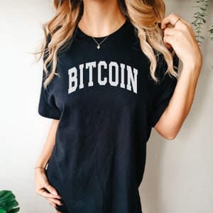 May include: A black t-shirt with the word "BITCOIN" printed in white, in a collegiate font.