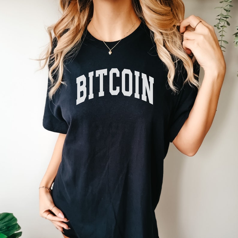 May include: A black t-shirt with the word "BITCOIN" printed in white, in a collegiate font.