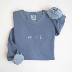 May include: A blue sweatshirt with the word "WIFE" embroidered on the front.