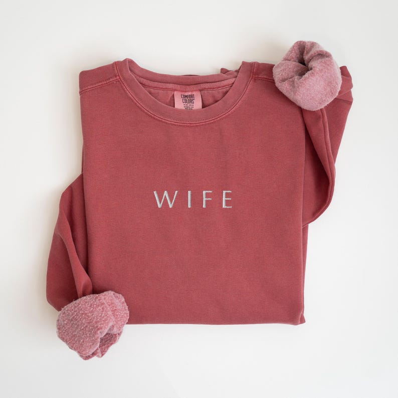 May include: A maroon sweatshirt with the word "WIFE" embroidered in white on the front.