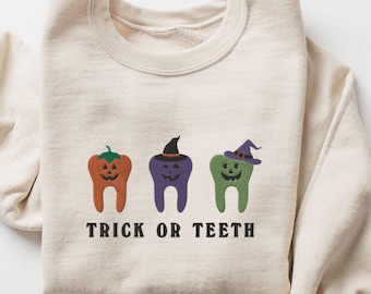 May include: A beige sweatshirt with a Halloween-themed design featuring three teeth with different colored hats and the text "Trick or Teeth".