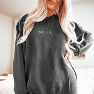 May include: A dark grey sweatshirt with the word "WIFE" printed in white on the front.