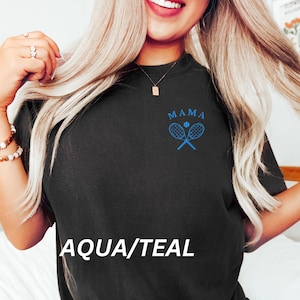 May include: A black t-shirt with the text "MAMA" and a blue tennis racket and ball graphic. The text "AQUA/TEAL" is printed below the graphic.