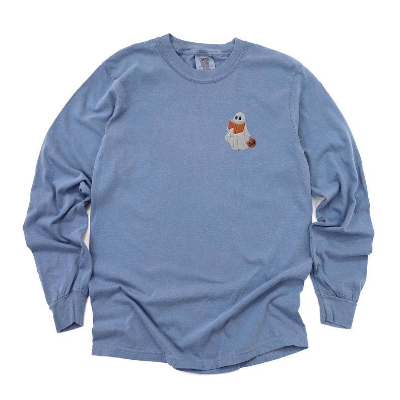 K&ouml;nnte beinhalten: Ein hellblaues Langarmshirt mit einem gestickten Geist, der ein Buch und einen K&uuml;rbis h&auml;lt.