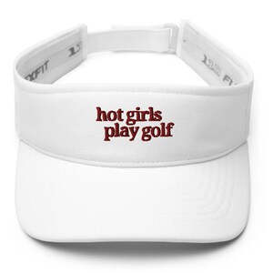 May include: White visor with the embroidered text "hot girls play golf" in a dark red color. The visor has an adjustable strap for a comfortable fit. The visor is designed to shield the eyes from the sun.