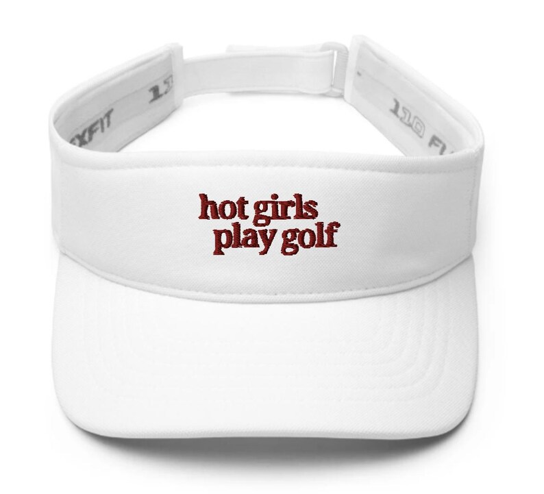 May include: White visor with the embroidered text "hot girls play golf" in a dark red color. The visor has an adjustable strap for a comfortable fit. The visor is designed to shield the eyes from the sun.
