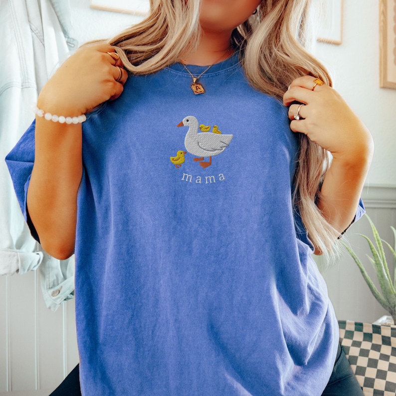 May include: A blue t-shirt with an embroidered image of a mama duck and her ducklings. The text "mama" is embroidered below the image.