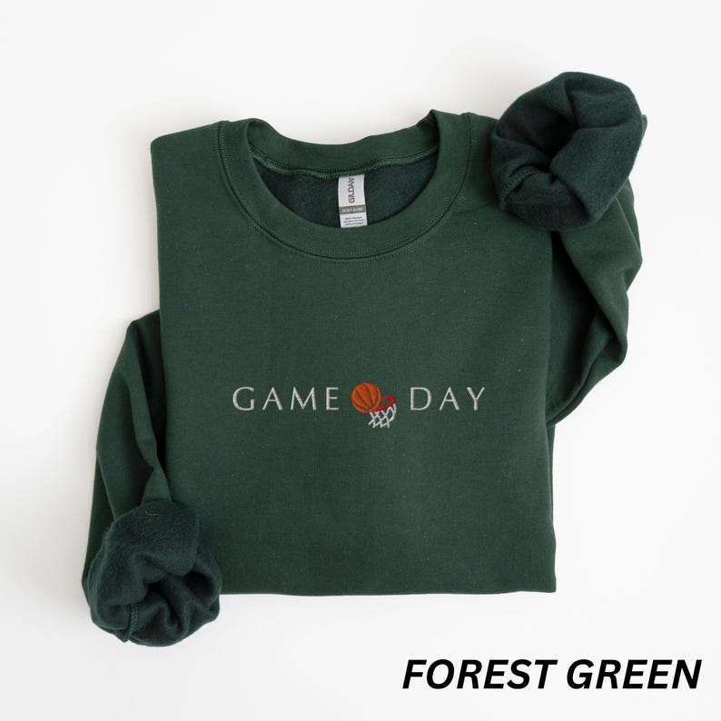 May include: Forest green sweatshirt with the text "GAME DAY" and a basketball graphic. The long-sleeved crewneck top is a solid color and has a soft, comfortable appearance. The sweatshirt is a casual style.