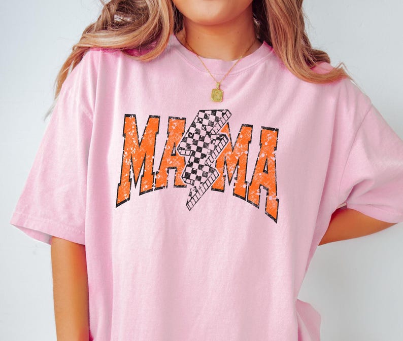 K&ouml;nnte beinhalten: Pinkes T-Shirt mit einem verwaschenen orangenen Grafikdruck des Wortes "MAMA" mit einem karierten Blitzdesign.