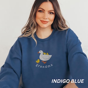 May include: Indigo blue sweatshirt with an embroidered image of a white duck with yellow ducklings and the word "grandma" underneath.