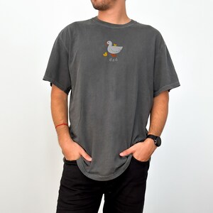 May include: Dark gray t-shirt with a duck and duckling graphic, and the word "dad" printed below. The shirt has short sleeves and a crew neck. The shirt is made of a soft, comfortable material.
