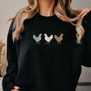 May include: Black sweatshirt with a row of three embroidered chickens in different colors: gray, white, and brown.