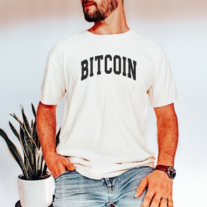 May include: A white t-shirt with the word "BITCOIN" printed in black, in an arched font style.