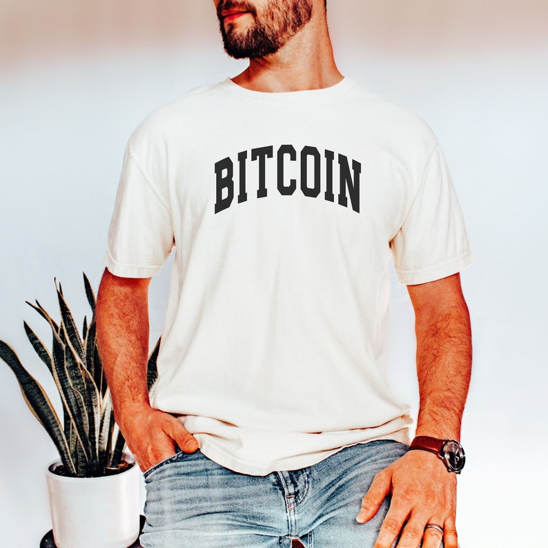 May include: A white t-shirt with the word "BITCOIN" printed in black, in an arched font style.