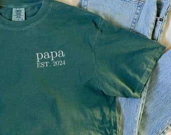 Puede incluir: Una camiseta verde oscuro con el texto "papa EST. 2024" bordado en la parte delantera.