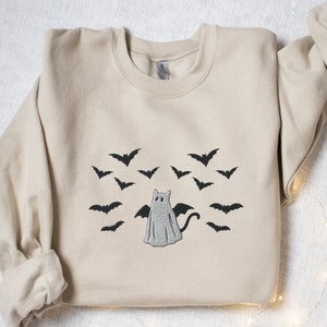 May include: A beige sweatshirt with an embroidered design of a ghost with bat wings and a cat tail surrounded by bats.