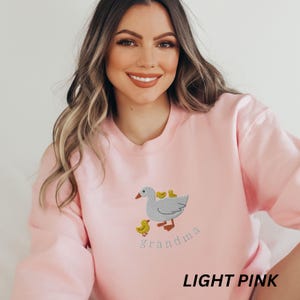 May include: Light pink sweatshirt with an embroidered goose and goslings design and the text "grandma".