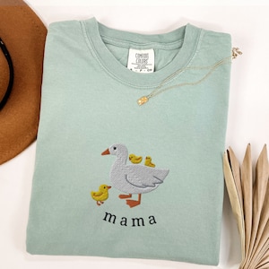 May include: A light blue t-shirt with an embroidered image of a goose and three goslings. The text "mama" is embroidered below the image.
