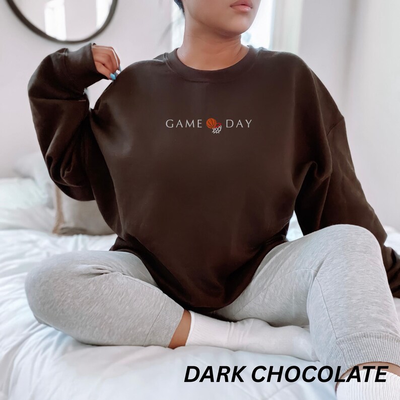 May include: Dark chocolate brown sweatshirt with the text "GAME DAY" and a basketball graphic. The sweatshirt is a crew neck style. The words "DARK CHOCOLATE" are printed at the bottom of the image.