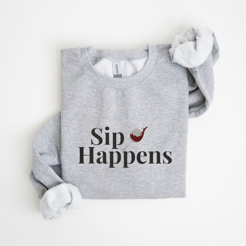 May include: Grey sweatshirt with the text "Sip Happens" and a small graphic of a wine glass with red wine.