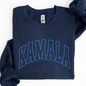 May include: A navy blue sweatshirt with a blue outline of the word "KAMALA" in a collegiate-style font.
