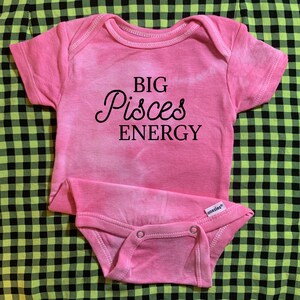 May include: Pink baby onesie with the text "BIG Pisces ENERGY" in black.
