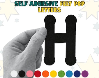 May include: Self-adhesive felt letter H in black. The letter is being held by a hand. The image also shows a variety of colors in felt circles.