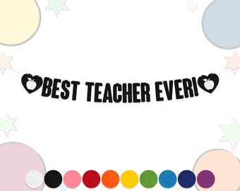 May include: A black banner with the text "BEST TEACHER EVER!" in bold white letters. The banner features a heart with an apple on each end. A row of colorful felt circles is at the bottom.