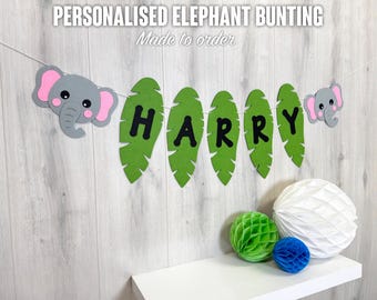 Könnte beinhalten: Ein personalisiertes Elefanten-Wimpel mit dem Namen "HARRY" auf grünen Blättern. Das Wimpel enthält graue Elefanten-Ausschnitte mit rosa Ohren. Der Text "PERSONALISED ELEPHANT BUNTING" und "Made to order" stehen oben.