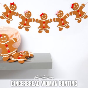 May include: A handmade gingerbread woman bunting with brown gingerbread women with pink and red accents hanging from a red string. The bunting is hanging on a white wall. The text "Handmade Gingerbread Woman Bunting" is printed below the bunting.