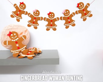 May include: A handmade gingerbread woman bunting with brown gingerbread women with pink and red accents hanging from a red string. The bunting is hanging on a white wall. The text "Handmade Gingerbread Woman Bunting" is printed below the bunting.