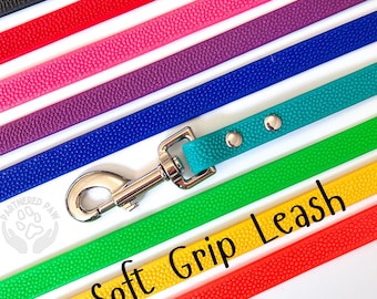 May include: A variety of colorful dog leashes in black, red, pink, purple, blue, teal, green, and yellow. Each leash has a textured surface and a silver metal clasp. The teal leash is connected to the clasp. The words "Soft Grip Leash" are in the image.