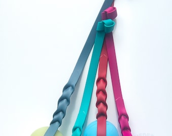 May include: Four colorful rubber dog toys with ropes attached. The toys are green, blue, purple, and yellow. The ropes are braided and have knots at the ends.