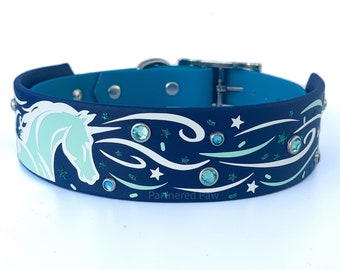 May include: A blue and teal dog collar with a white unicorn and stars design. The collar has teal rhinestones and the text "Partnered Paw" on the bottom.