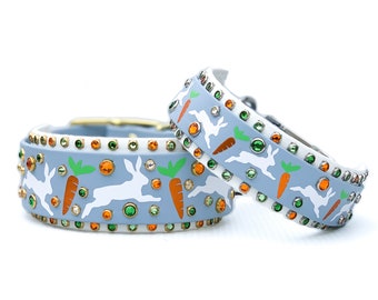 May include: Two light blue dog collars with white bunnies and orange carrots, decorated with rhinestones and green gems.