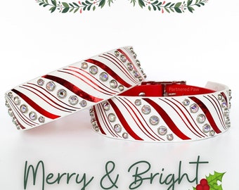 May include: Two white and red candy cane patterned dog collars with clear rhinestones. The collars are layered on top of each other. The text "Partnered Paw" is on the bottom collar. The text "Merry & Bright" is at the bottom of the image with a green holly sprig with red berries.