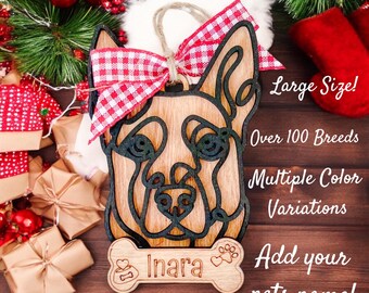 May include: A wooden Christmas ornament shaped like a dog's head with a red and white checkered bow. The ornament has a bone-shaped tag with the name "Inara" on it. The text "Large Size! Over 100 Breeds Multiple Color Variations Add your pets name!" is visible in the image.
