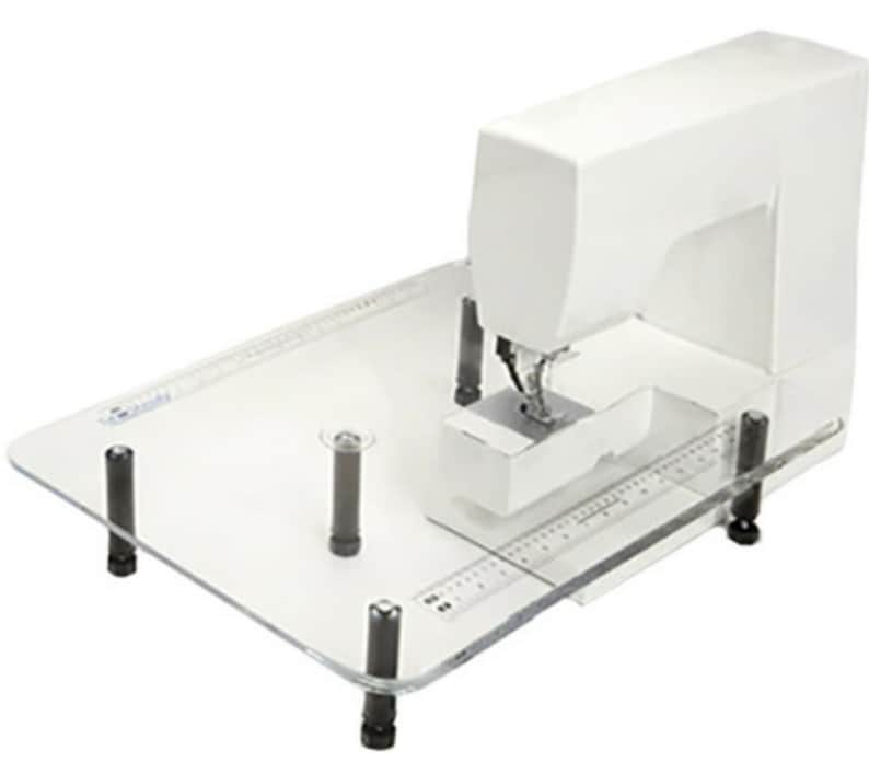 May include: A white sewing machine on a clear acrylic sewing table with four black legs. The table has a ruler printed on it.