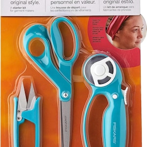 May include: A Fiskars garment making starter kit in retail packaging containing a pair of teal-handled scissors, a teal-handled rotary cutter, and a pair of teal-handled thread snips. The packaging features the text Show off your original style.