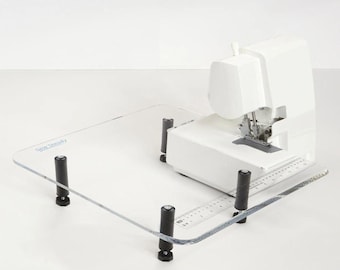 May include: A clear acrylic sewing machine table with four black adjustable legs. The table has a ruler printed on the surface and the text "Sew Steady" printed on the top left corner. A white sewing machine is sitting on the table.