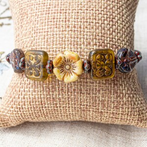 May include: A bracelet made with brown, yellow, and blue glass beads, and a white flower-shaped bead.