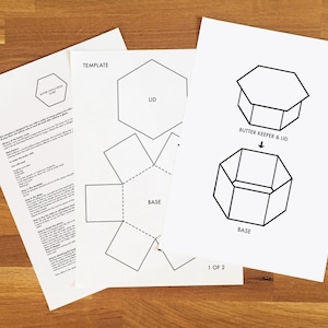 Könnte beinhalten: Eine druckbare Vorlage für einen sechseckigen Butterbehälter und einen Deckel. Die Vorlage enthält Anweisungen zum Zusammenbauen des Butterbehälters und des Deckels. Die Vorlage ist mit "1 von 2" gekennzeichnet.