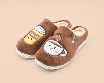 May include: A pair of brown plush slippers with a white interior lining and white soles. One slipper features an embroidered yellow coffee cup with the text COFFEE, while the other displays a white coffee mug with steam and a small black COFFEE tag.