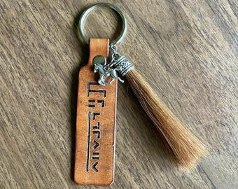 May include: A brown leather keychain with a horse charm and a brown horsehair tassel. The leather tag has the text "I'll be there" engraved on it.