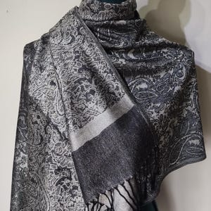 May include: A black and white patterned scarf with a fringe. The scarf is draped over a mannequin.